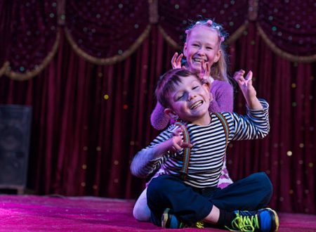 Two funny playful children, boy and girl, smiling while acting as monsters with claws, on a purple stage, in a theatrical representation