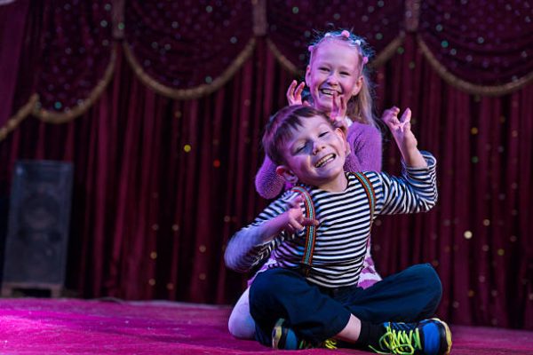 Two funny playful children, boy and girl, smiling while acting as monsters with claws, on a purple stage, in a theatrical representation