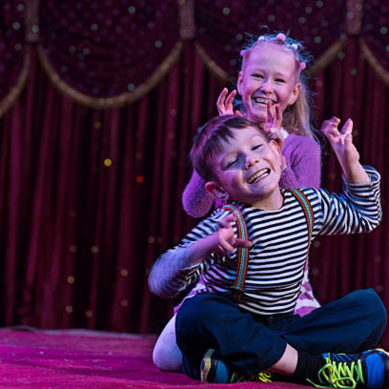 Two funny playful children, boy and girl, smiling while acting as monsters with claws, on a purple stage, in a theatrical representation